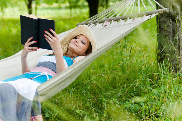 Gelukkig jonge vrouw lezen in hangmat in groen park buiten - Foto, afbeelding
