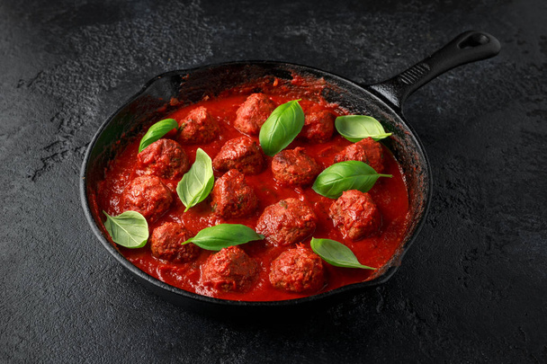 Homemade Meatballs in iron cast with sweet and hot tomato sauce, basil. On wooden table - Photo, Image
