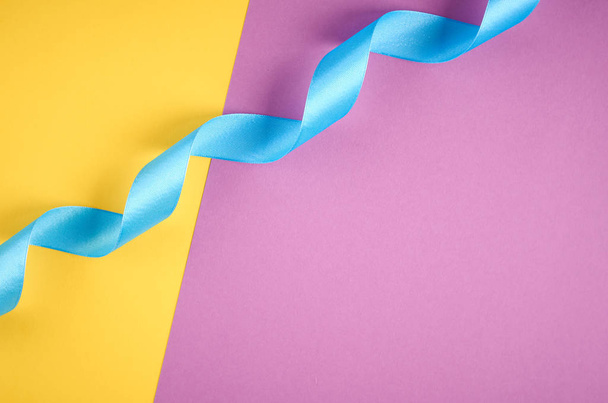 Blue ribbon on purple and yellow background composition, flat lay - Фото, зображення