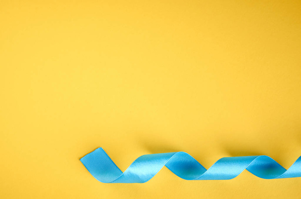 Blue ribbon on yellow background composition, flat lay - Foto, imagen