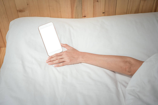 Kobieta trzyma na swoim smartfonie śpiąc w tle łóżka - Zdjęcie, obraz