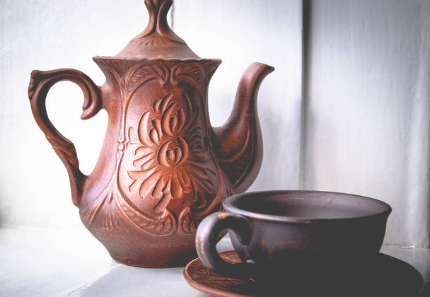 Um bule de chá e uma xícara de barro estão perto da janela
. - Foto, Imagem