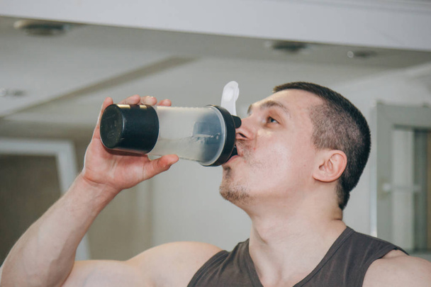 the athlete drinks water from a shaker in the training center. rest between exercises in the gym - Foto, Imagem
