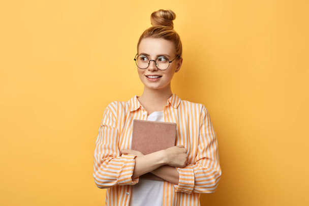 Happy young beautiful woman with hairbun standing and holding folder - Фото, изображение