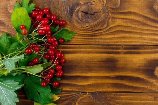 木製のテーブルの上に緑の葉と赤いビバーナムベリー。トップビュー - 写真・画像