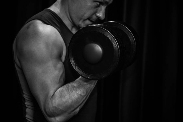athlete trains biceps hands with dumbbells in the center of workouts on a black background. training tools in the gym close-up - Foto, imagen