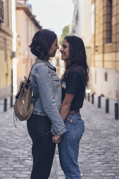 Jovens mulheres atraentes casal lésbico olhando e sorrindo uns aos outros em uma rua de Madrid. Cena de amor real
. - Foto, Imagem