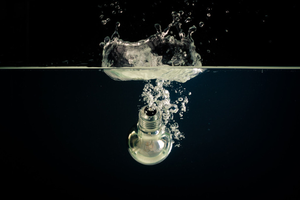 Une ampoule tombant dans l'eau claire avec un fond sombre
 - Photo, image