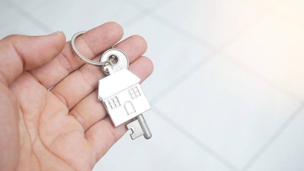 Мужчина держит ключ с домашней безделушкой на светлом фоне, концепция недвижимости
 - Фото, изображение
