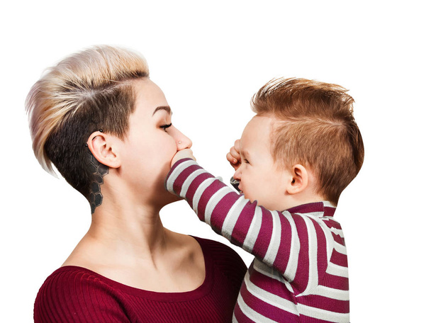 Надзвичайна мати з маленьким хлопчиком на руках з зачіскою посміхається, ізольована на білому тлі. Маленький хлопчик грає з мамою і закриває рот
. - Фото, зображення