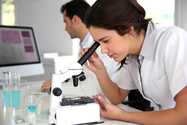 Young woman looking through microscope lense - Foto, imagen