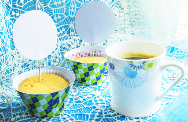 Dos cupcakes en una servilleta azul con bordado de encaje, una taza de café, el espacio de una copia de la tarjeta, la ubicación de las tarjetas y las invitaciones a las vacaciones
 - Foto, Imagen