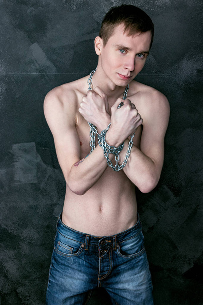 Handsome skinny guy holding a chain. Black background - 写真・画像