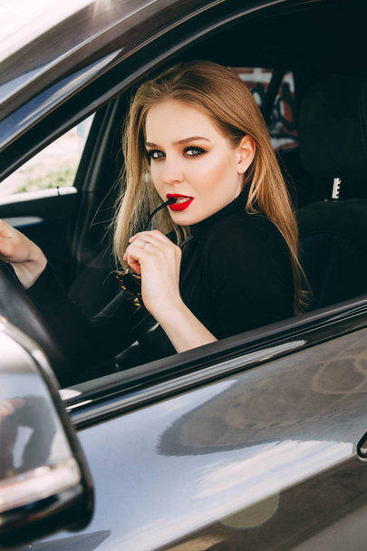 Young stylish woman with red lips sitting in car - Zdjęcie, obraz
