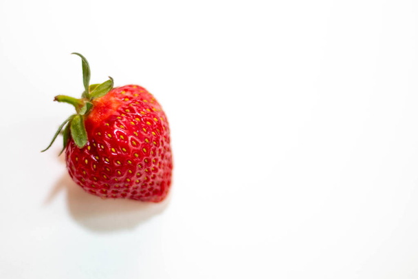 One beautiful red strawberry with a green tail lies on a white background. Isolate - Φωτογραφία, εικόνα