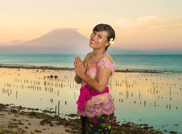 beautiful happy middle aged Indonesian Balinese woman in traditional ceremony dress at tropical beach with Bali Agung volcano background in holidays tourist destination - Fotoğraf, Görsel