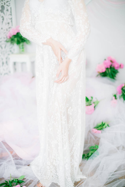 Beautiful young girl in a white lace dress with peony flowers in a bright studio - Photo, Image