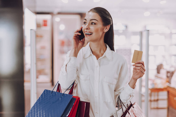 Merry young lady is speaking on phone while shopping - Foto, Imagen