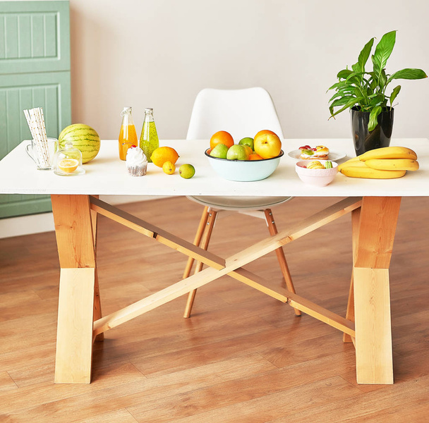 Fruits: apples, watermelon, pineapple, bananas, lemons, oranges on the table, warm loft-style kitchen - Фото, зображення