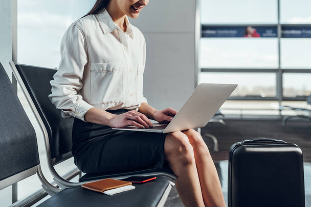 Joyful woman is using laptop before flight - Фото, зображення
