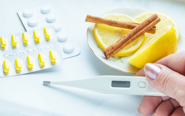 Thermometer in handen, tabletten, citroen met kaneel, het concept van de behandeling van verkoudheid - Foto, afbeelding