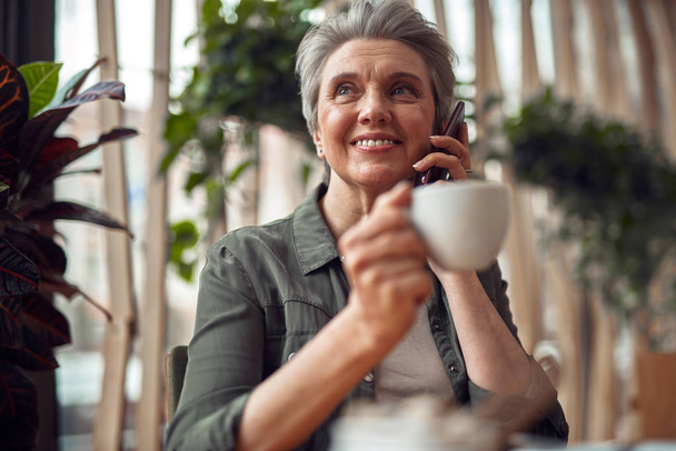 Happy aged woman talking on mobile phone in cafe - Photo, image