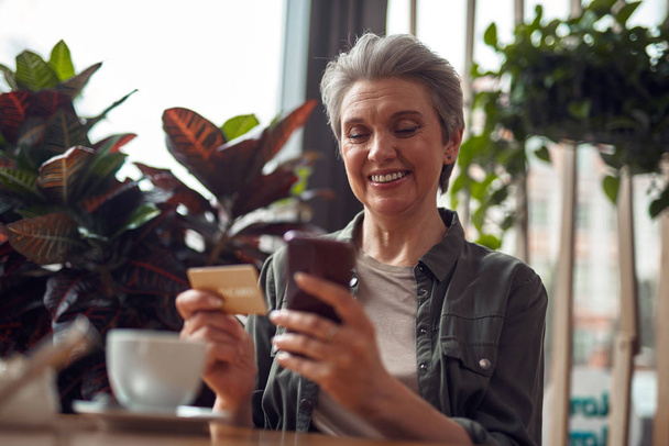 Happy aged woman with phone and credit card - Valokuva, kuva