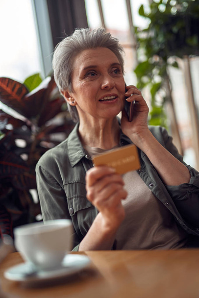 Careful aged woman talking by phone in cafe - Foto, Imagem