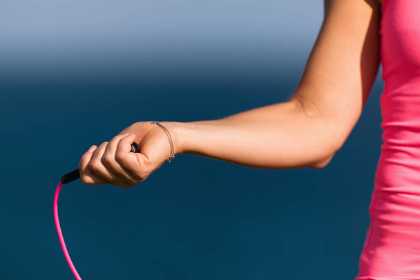 Sportlerin hält Springseil in der Hand turnt vor dem Hintergrund der Meeresküste - Foto, Bild