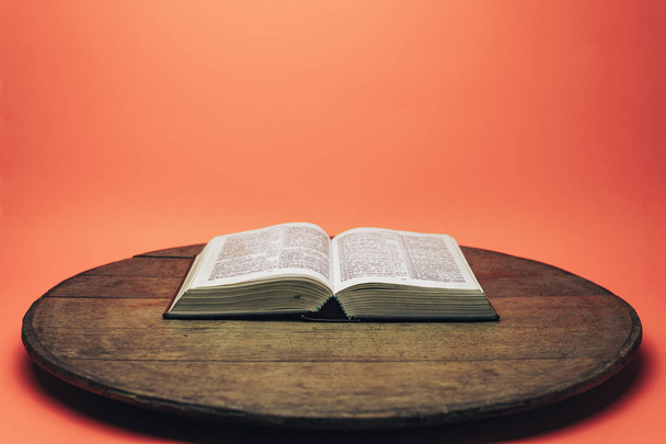 Bible and the crucifix beads on a old round table. Beautiful coral orange background. Religion concept. - Photo, Image