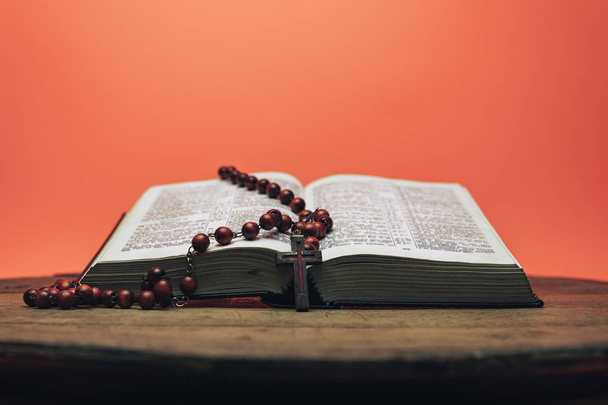 La Biblia y las cuentas del crucifijo en una vieja mesa redonda. Hermoso fondo naranja coral. Concepto de religión
. - Foto, Imagen