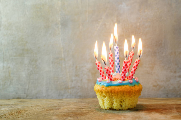 narozeninový Muffin nebo dort s červenými a modrými hořící svíčkami na dřevěné desce proti rustikální stěně, kopírovat prostor - Fotografie, Obrázek