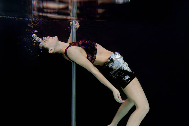 junge, fitte, schlanke Frau mit Stange unter Wasser im Schwimmbad auf schwarzem Hintergrund - Foto, Bild