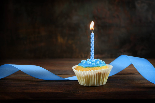 Muffins oder Cupcakes mit blauer brennender Kerze und Schleife auf dunklem Holzbrett vor braunem, rustikalem Hintergrund, Geburtstags- oder Weihnachtskonzept mit Kopierraum - Foto, Bild