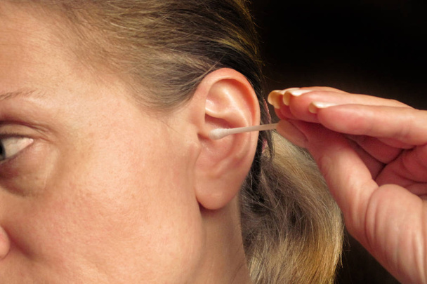 Женщина средних лет чистит ухо ватным тампоном или палкой
 - Фото, изображение
