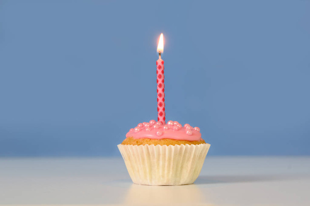 Muffin nebo dortík s růžovou hořící svíčkou proti modrému pozadí, koncepce narozenin s velkým místem kopírování - Fotografie, Obrázek