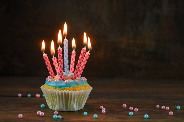 birthday muffin or cupcake with red and blue burning candles and sugar balls on a rustic wooden board against a dark brown background, copy space - Φωτογραφία, εικόνα