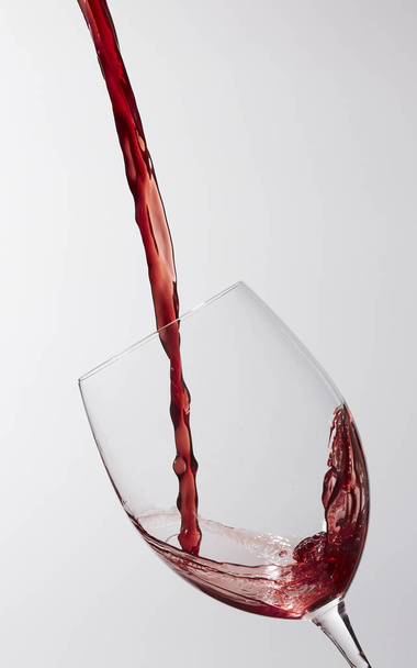 A stream of red wine being poured into a wineglass held on an angle on a gray background - Photo, Image