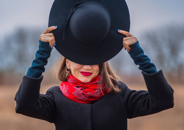 Dívka v černém kabátě, lopatka s červenou rtěnky na rtech, chodí do parku. Styl a moderní móda. - Fotografie, Obrázek