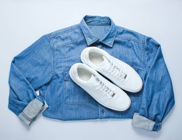 Flat lay style white hipster sneakers with denim shirt on gray background. Retro culture, top view - Photo, Image
