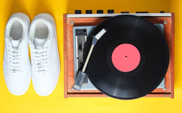 Pop kültürü. Beyaz hipster Sneakers, sarı arka planda vinil oyuncu. Retro tarzı. 80s. üst görünüm, minimalis - Fotoğraf, Görsel