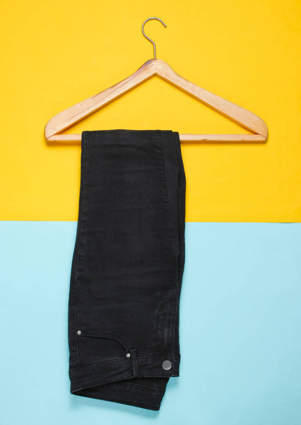 Vista superior, pantalones vaqueros planos de color negro con una percha de madera sobre un fondo pastel. Minimalismo
 - Foto, imagen