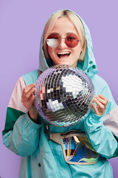 Woman with sparkling disco ball, dressed in trendy mint and pink windbreaker. - Foto, imagen