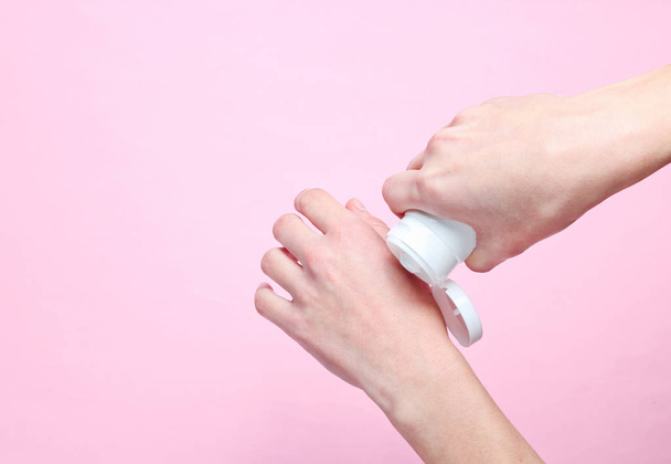 Hand care. Woman holding cream tube and applying moisturizer cream on her beautiful hands for soft hand skin on pink pastel background. Top view, minimalism, flat lay - Zdjęcie, obraz
