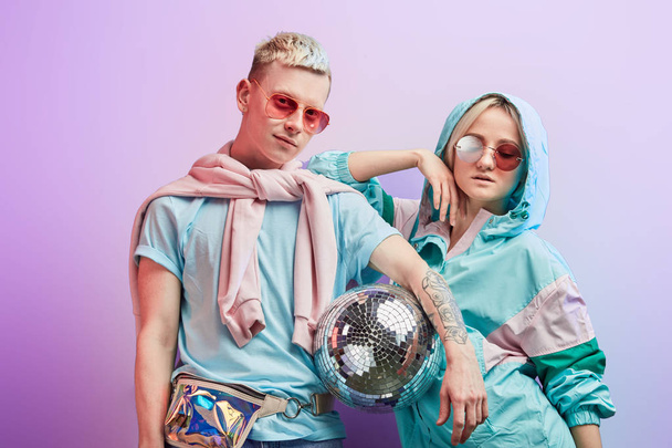 Young fashionable couple of dancers posing with disco ball on violet background - Foto, Bild