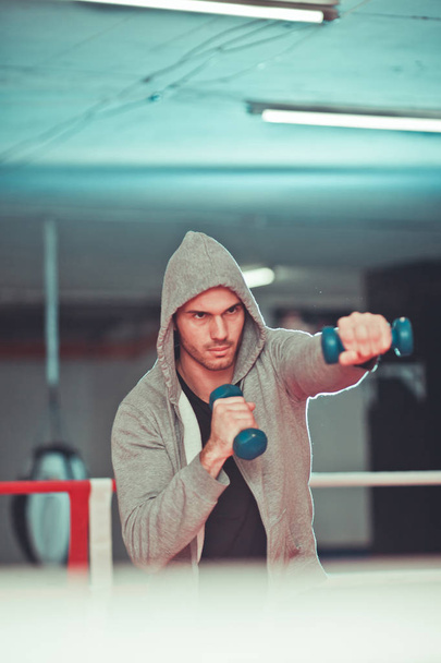 Concepto de boxeo. Hombre boxeador durante el ejercicio de boxeo haciendo impacto directo con pesas en el ring de boxeo
 - Foto, imagen