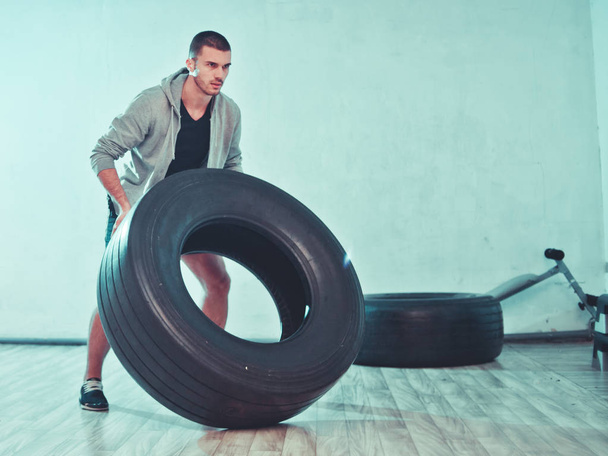 Young sports man raises a large weight wheel. training process. Functional trainin - Fotoğraf, Görsel