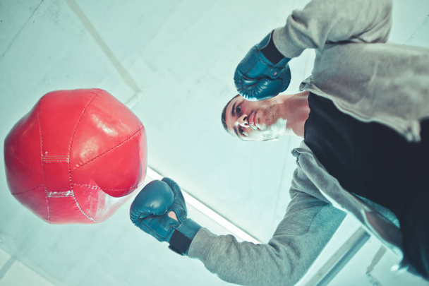 Красавчик боксер тренирует удары руками боксерской грушей. Нижний вид
. - Фото, изображение