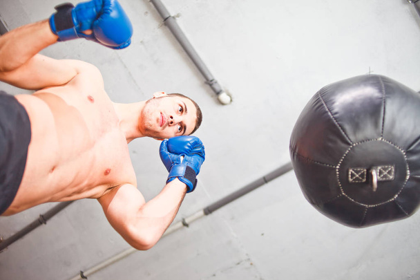 Un beau boxeur de sport entraîne des coups de poing à la main avec un sac de boxe. Vue du bas
. - Photo, image