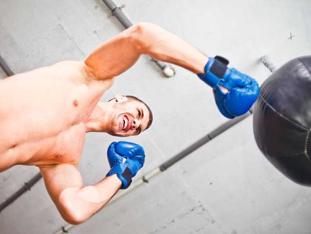 El guapo boxeador deportivo entrena puñetazos de mano con un saco de boxeo. Vista inferior
. - Foto, Imagen